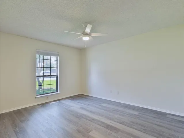 an empty room with wooden floor ceiling fan and windows
