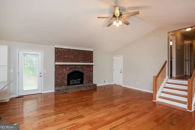 a view of an empty room with wooden floor fireplace and a window