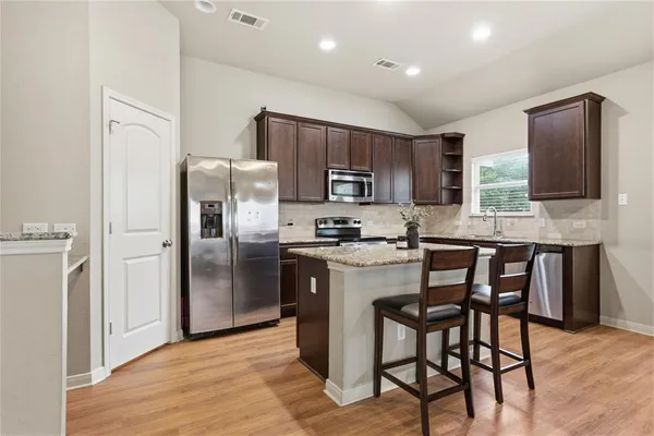 a kitchen with stainless steel appliances granite countertop a refrigerator a stove a sink a dining table and chairs