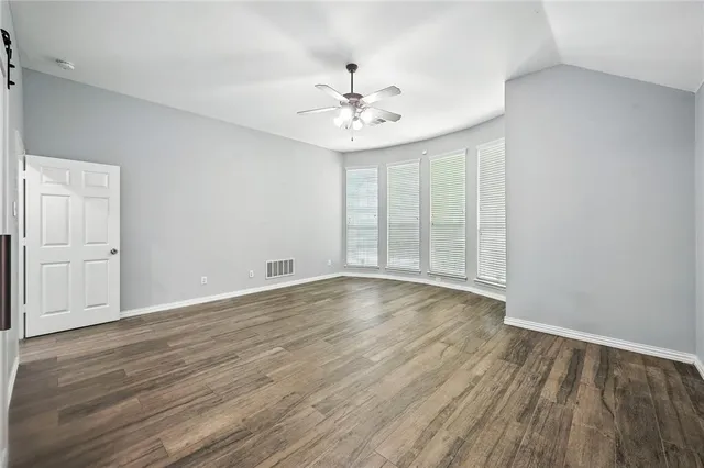 an empty room with wooden floor fan and windows