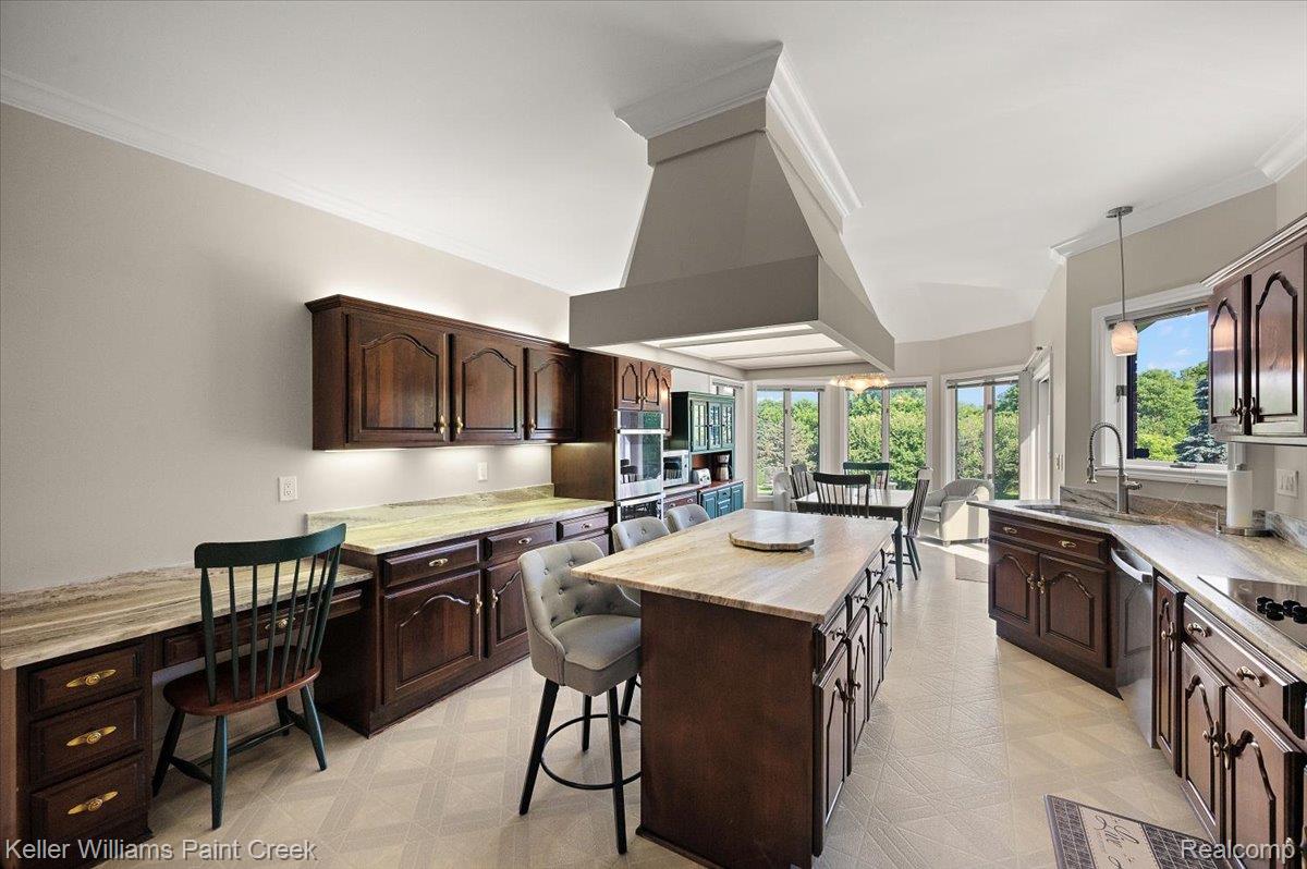 69069 Campground Road Romeo, MI 48065 - Photo 32 of 78 Spacious kitchen featuring an expansive center island, integrated desk area, dark wood cabinetry, light-toned countertops, and ceiling crown molding