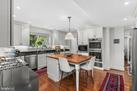 a kitchen with stainless steel appliances granite countertop a stove a sink dishwasher a refrigerator and white cabinets with wooden floor