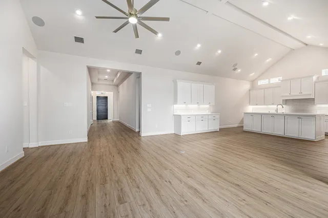 a view of an empty room with wooden floor and a kitchen
