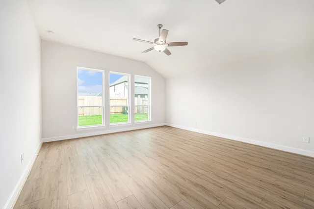 an empty room with wooden floor fan and windows