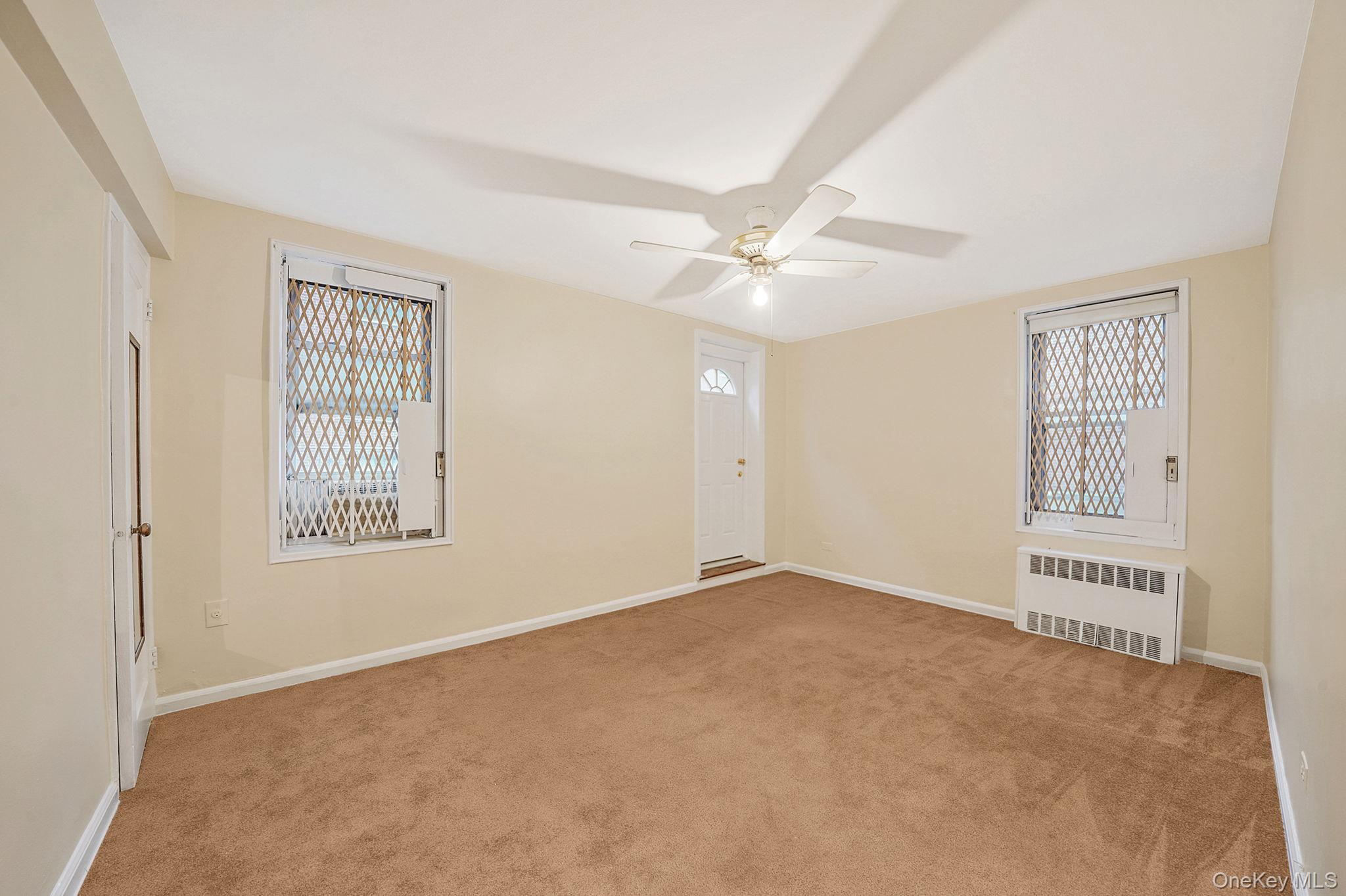35-40 75th Street, Unit 1B Queens, NY 11372 - Photo 12 of 19 Spare room featuring light carpet, radiator heating unit, and ceiling fan