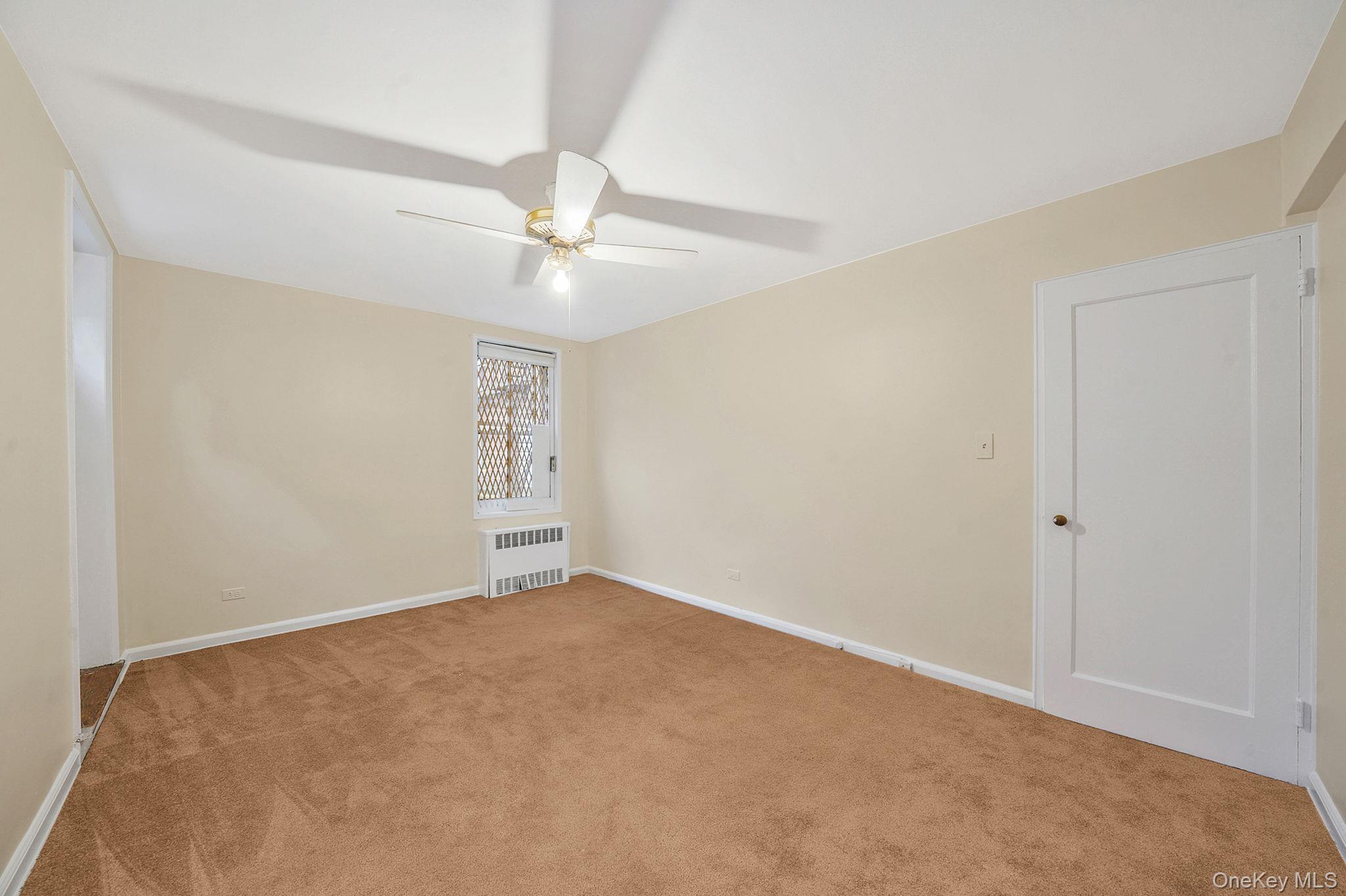 35-40 75th Street, Unit 1B Queens, NY 11372 - Photo 14 of 19 Empty room with light colored carpet, radiator heating unit, and ceiling fan