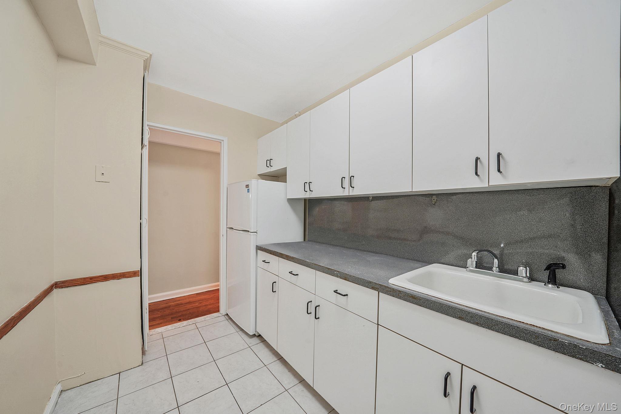 35-40 75th Street, Unit 1B Queens, NY 11372 - Photo 16 of 19 Kitchen with dark countertops, light tile patterned flooring, white cabinets, and freestanding refrigerator