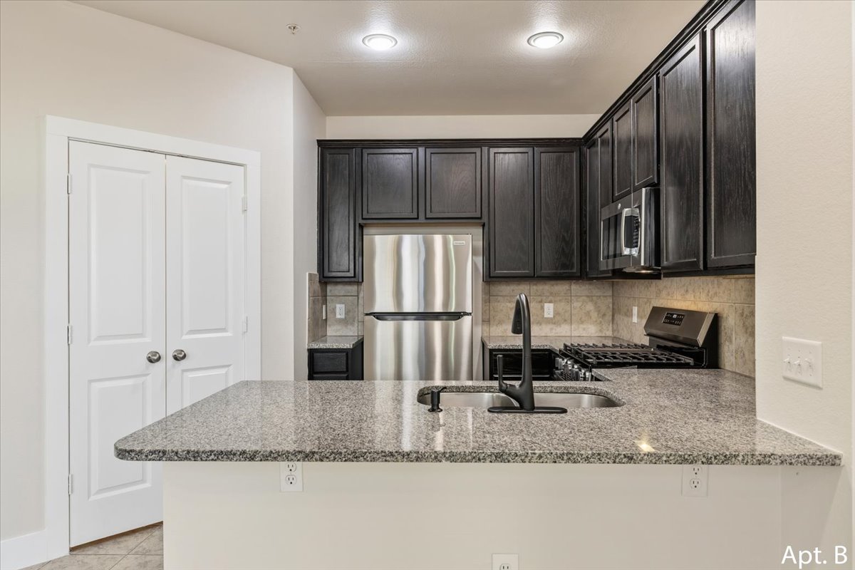 2225 Katy Lane, Unit B Georgetown, TX 78626 - Photo 9 of 22 Kitchen featuring stainless steel appliances, a peninsula, light stone countertops, decorative backsplash, and light tile patterned flooring