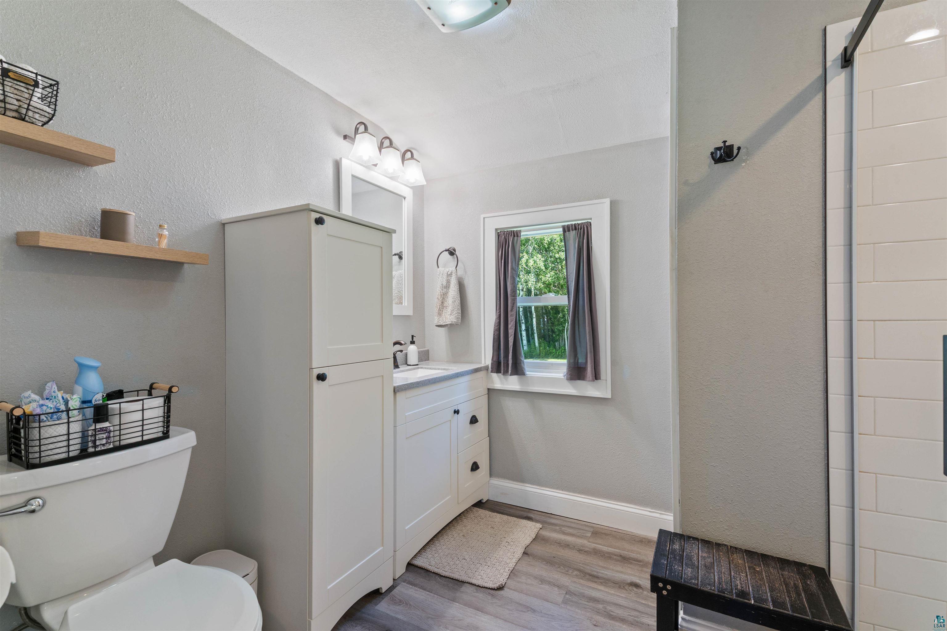 3835 South County Rd K South Range, WI 54874 - Photo 5 of 29 Bathroom with wood-finish flooring, white vanity with integrated sink, white storage cabinet, and a white subway tile shower