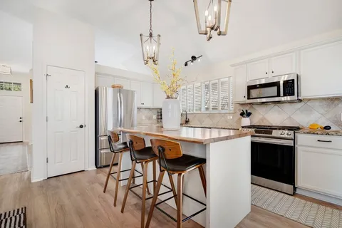 a kitchen with stainless steel appliances granite countertop a stove top oven a refrigerator a sink and a dining table with wooden floor