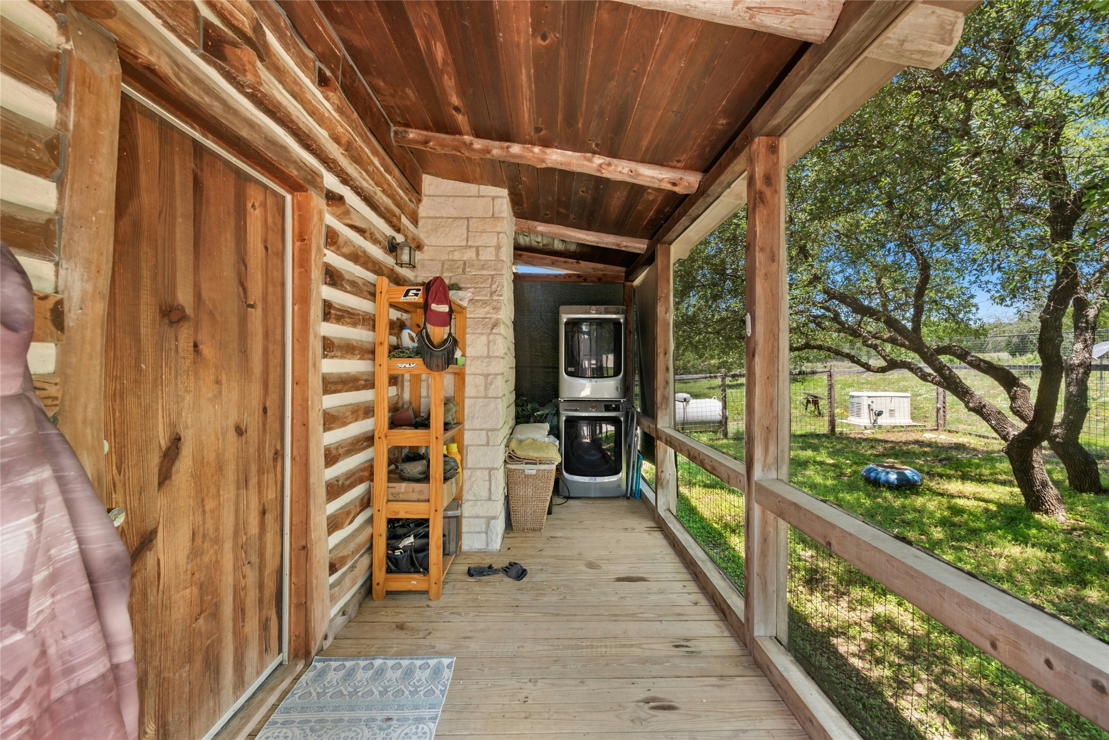 496 Middleton Road Spicewood, TX 78669 - Photo 8 of 40 Covered wood-plank porch with a natural wood railing, stone-clad accent wall, and stacked laundry appliances