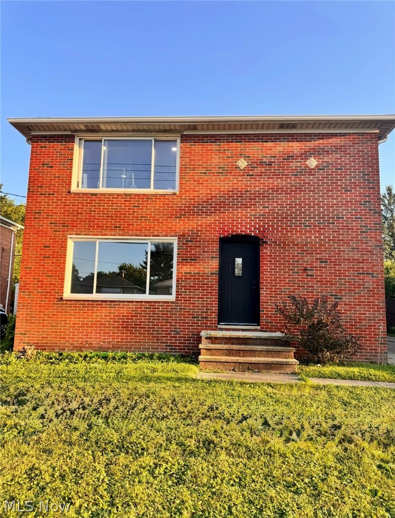 View of front of home featuring brick siding, entry steps, and a front yard