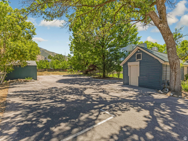 12825 South Fort Street Draper, UT 84020 - Photo 39 of 52 Paved parking area framed by mature trees, featuring a blue-sided outbuilding with a light-colored door and a dark green shed