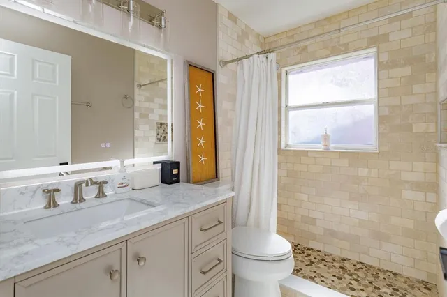 a bathroom with a granite countertop sink a toilet a mirror and shower