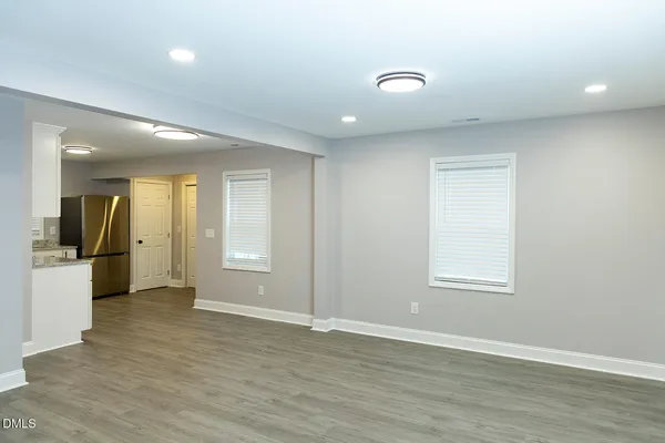 an empty room with wooden floor and a kitchen