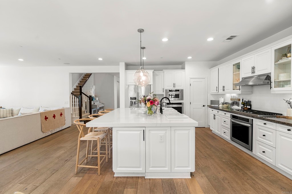 7001 Sitio Frontera Carlsbad, CA 92009 - Photo 16 of 40 a kitchen with stainless steel appliances kitchen island granite countertop a stove top oven a sink a dining table and chairs with wooden floor