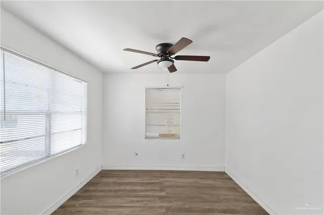 an empty room with wooden floor chandelier fan and windows