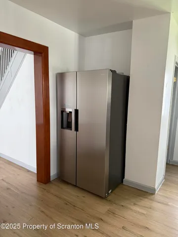 a view of a refrigerator in kitchen and an empty room with wooden floor