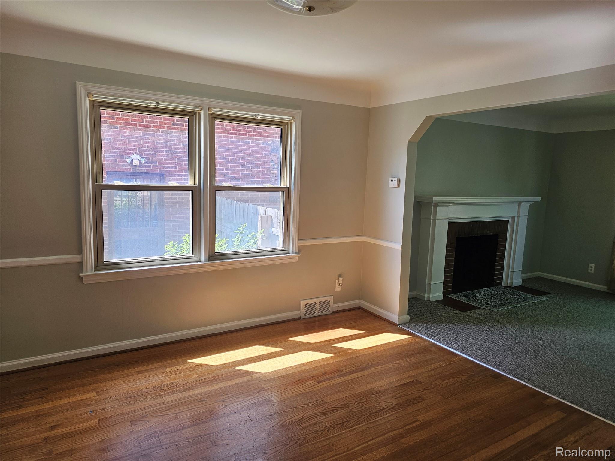 5240 Harvard Road Detroit, MI 48224 - Photo 9 of 18 Hardwood flooring extends from a double window with white trim, complemented by chair rail molding on the walls