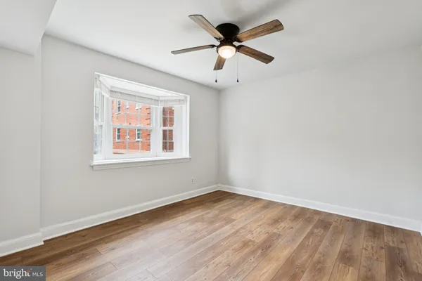 an empty room with wooden floor ceiling fan and windows
