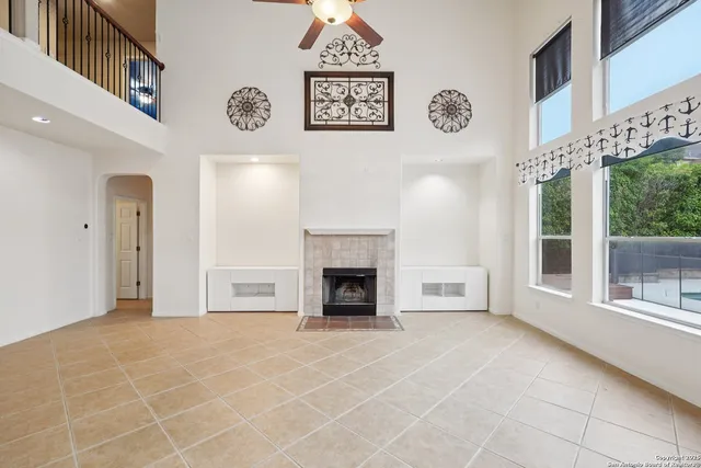 a view of a livingroom with a fireplace a ceiling fan and windows