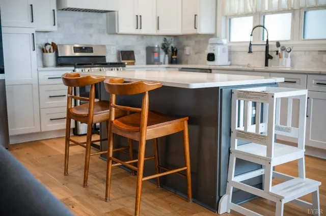 a kitchen with stainless steel appliances granite countertop a stove top oven a refrigerator a sink and white cabinets with wooden floor