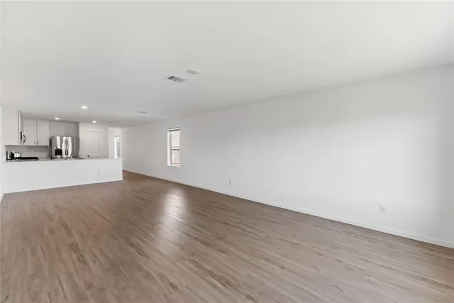 a view of an empty room with wooden floor and a kitchen