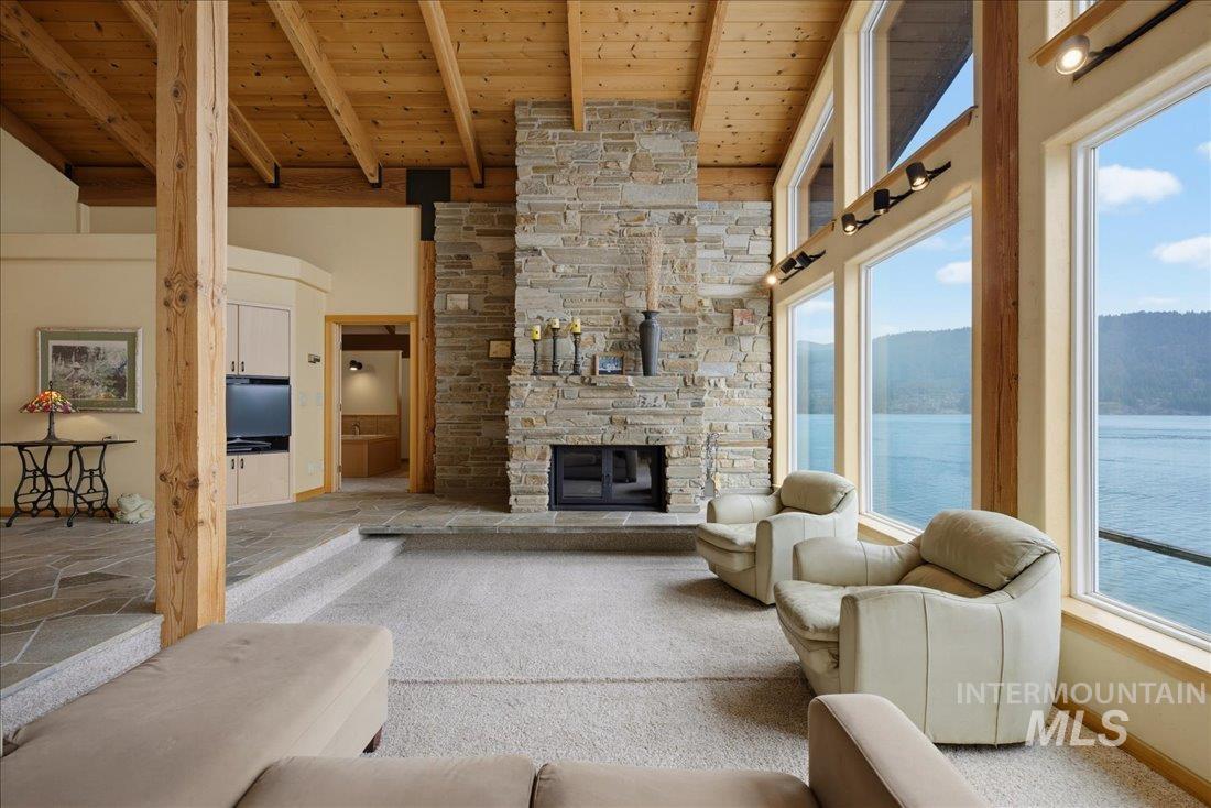 3800 Warren Wagon Road McCall, ID 83638 - Photo 9 of 50 Living area featuring a stone-clad fireplace, exposed wood beam ceiling, floor-to-ceiling windows, and a raised flagstone floor entry