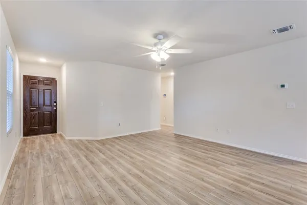 a view of an empty room with chandelier fan and wooden floor