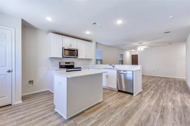 a kitchen with stainless steel appliances a stove top oven a sink a refrigerator white cabinets and wooden floor