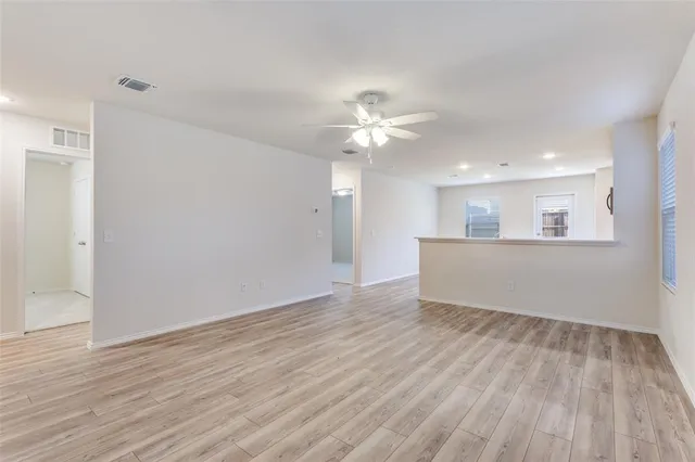 a view of an empty room with wooden floor and a kitchen