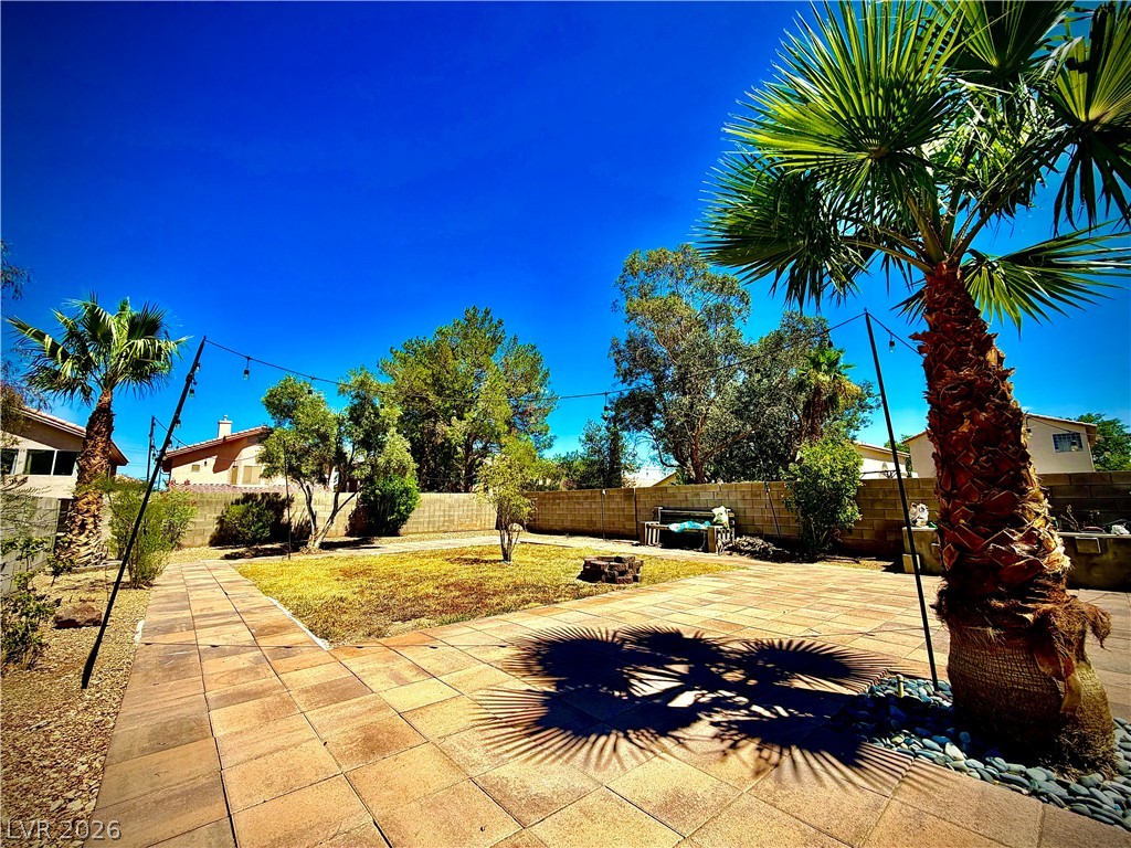 3936 Gold Point Street Las Vegas, NV 89129 - Photo 21 of 23 A well-maintained paved patio extends into a verdant lawn, framed by lush trees and a clear blue sky.