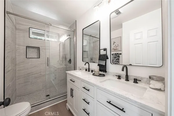 a bathroom with a granite countertop sink toilet a mirror a glass door and shower