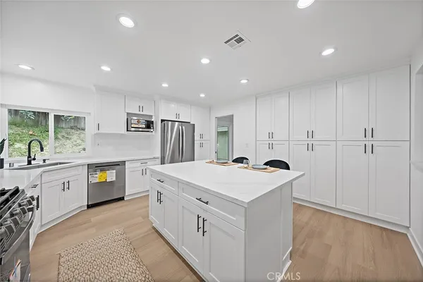 a kitchen that has a lot of white cabinets and stainless steel appliances