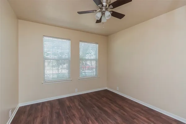 an empty room with wooden floor fan and windows