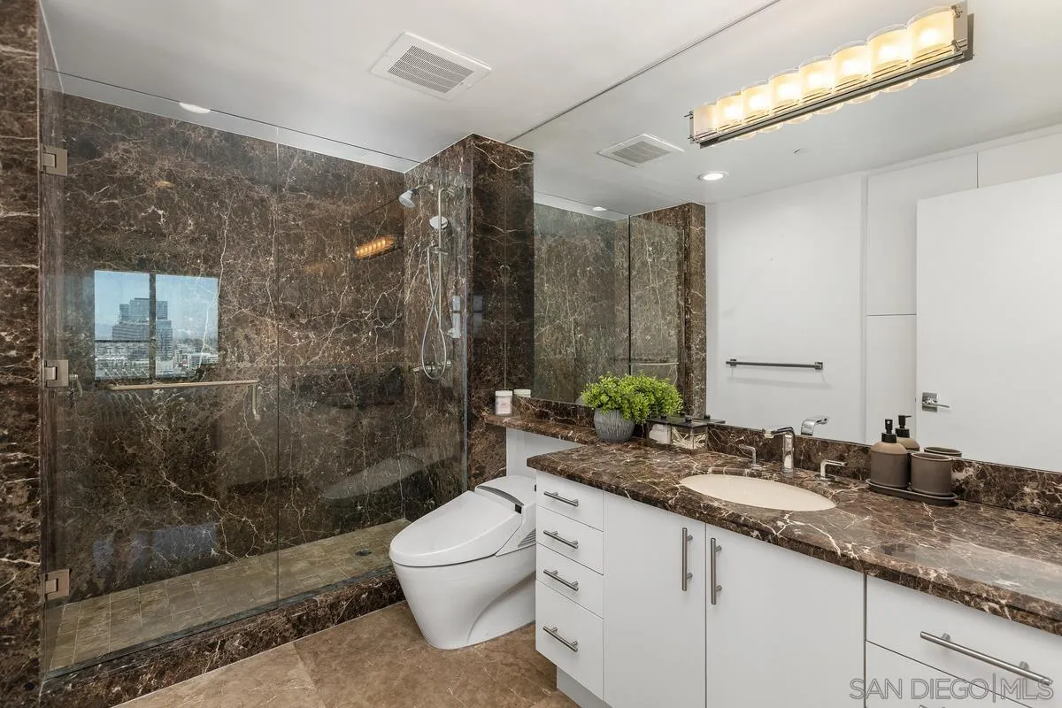 645 Front Street, Unit 2004 San Diego, CA 92101 - Photo 24 of 47 a bathroom with a granite countertop sink a toilet a mirror and shower