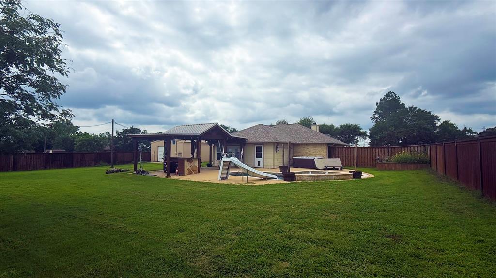 1356 Kerry Lane Azle, TX 76020 - Photo 23 of 27 Expansive backyard featuring a large grass area, a built-in outdoor kitchen under a covered pergola, a concrete patio, and a hot tub