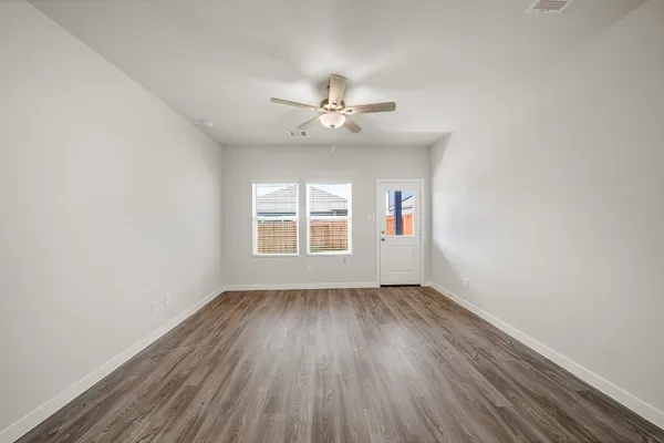 an empty room with wooden floor ceiling fan and windows