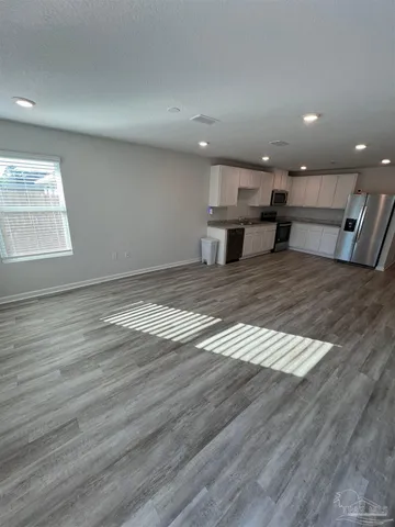 a view of an empty room with wooden floor and kitchen