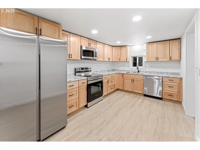 a kitchen with stainless steel appliances granite countertop a stove top oven a sink and white cabinets with wooden floor