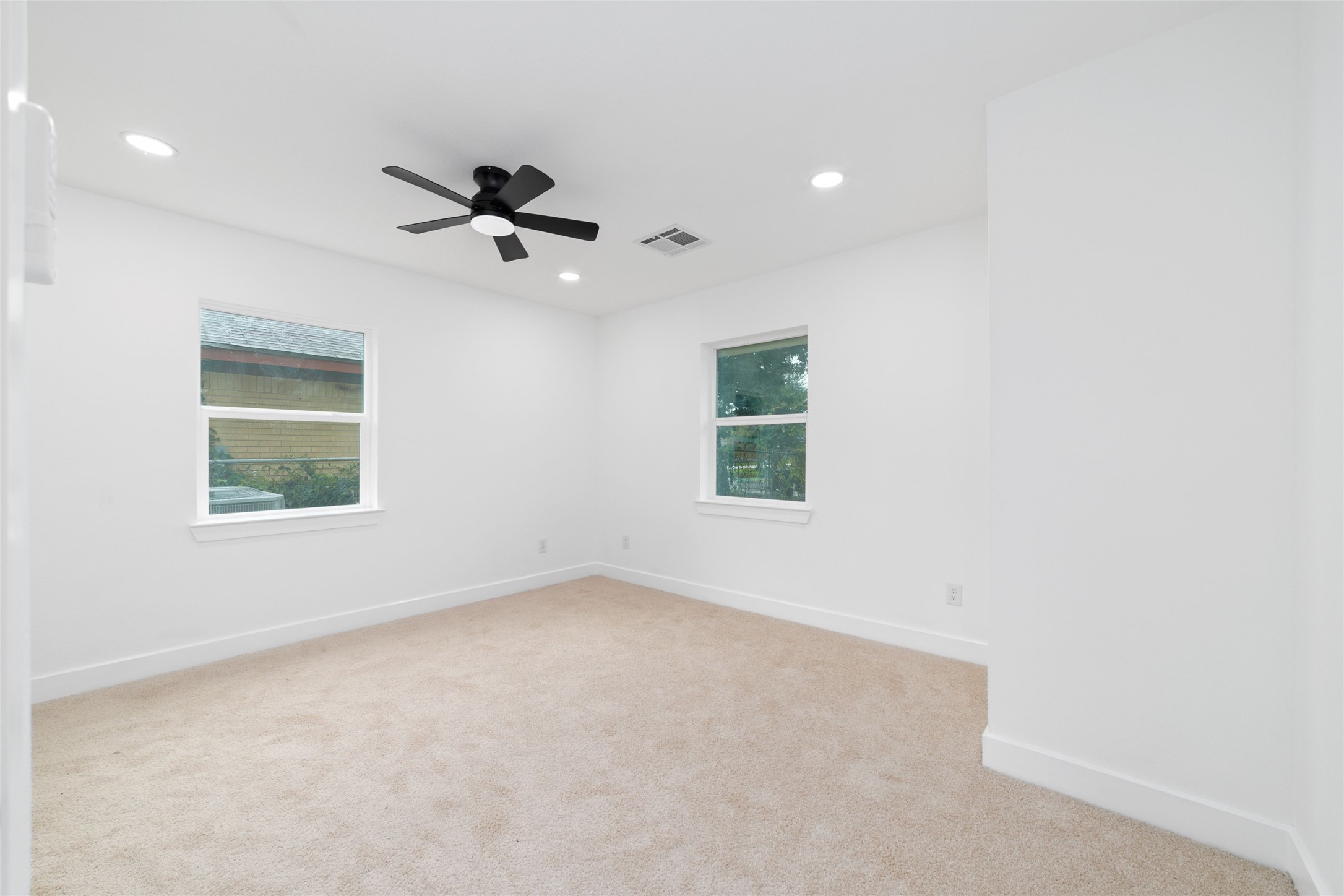 5709 Langley Road Houston, TX 77016 - Photo 14 of 27 The Master Bedroom is bright and airy with neutral walls and carpet, featuring two windows for natural light, recessed lighting, and a ceiling fan for comfort.