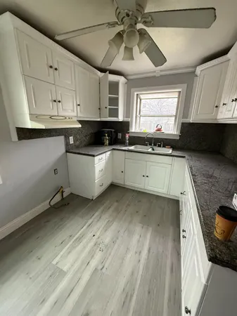 a kitchen with a sink dishwasher and white cabinets with wooden floor