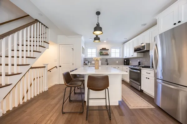 a kitchen with granite countertop a refrigerator a stove a sink dishwasher and white cabinets with wooden floor