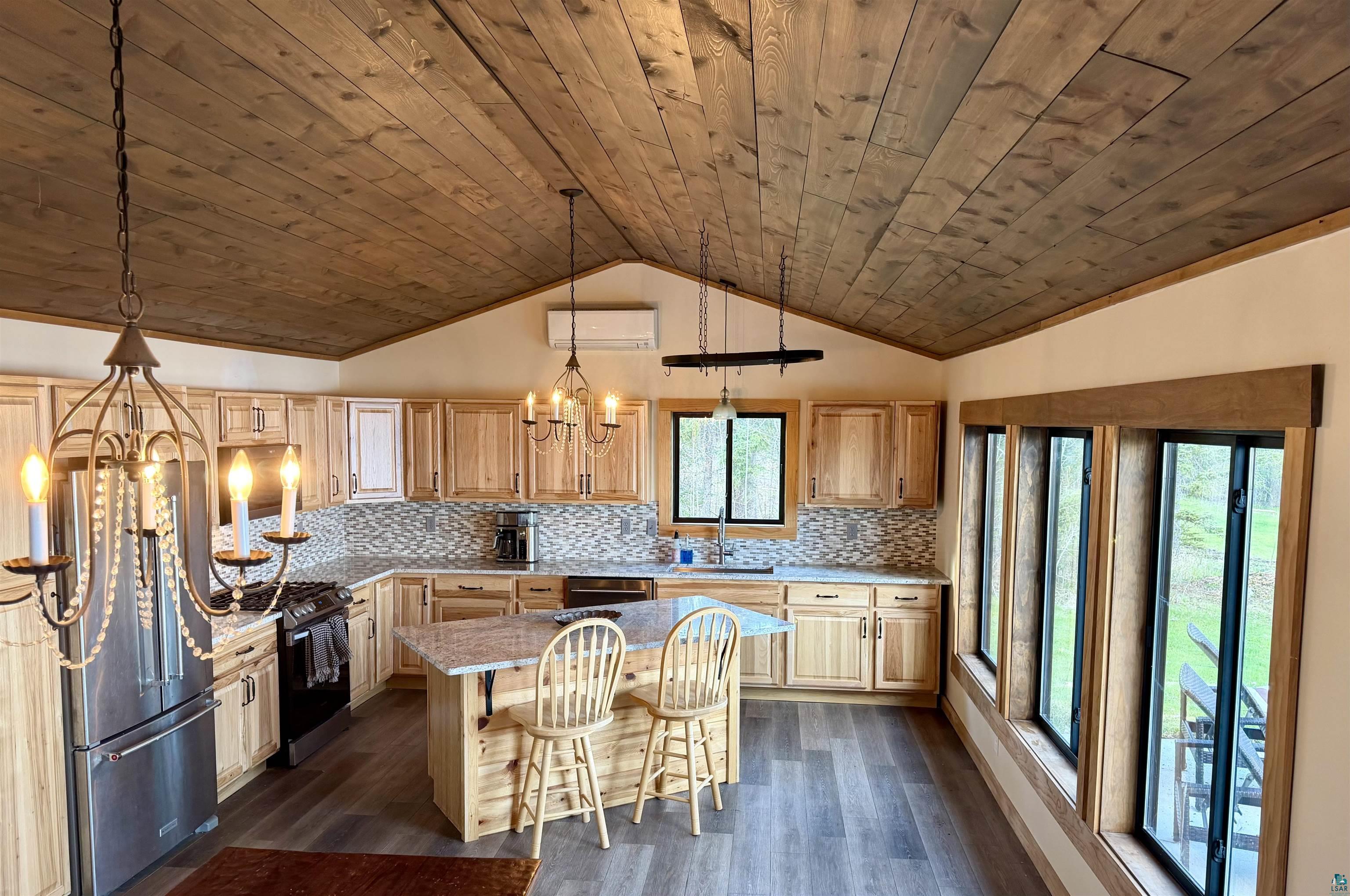 5274 Marble Lake Road Two Harbors, MN 55616 - Photo 17 of 79 Vaulted wood-finish ceiling extending over a kitchen featuring light wood cabinetry, a granite island, stainless steel appliances, and a mosaic tile backsplash