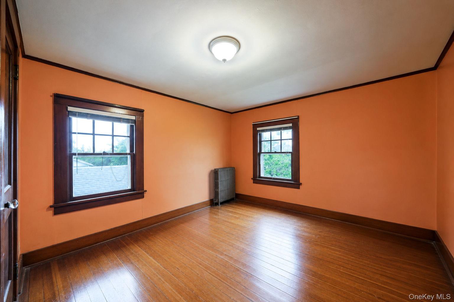1055 Oregon Road Mattituck, NY 11952 - Photo 25 of 33 Room featuring wood-finish flooring, two sash windows with wood trim, a flush mount ceiling light fixture, and crown molding