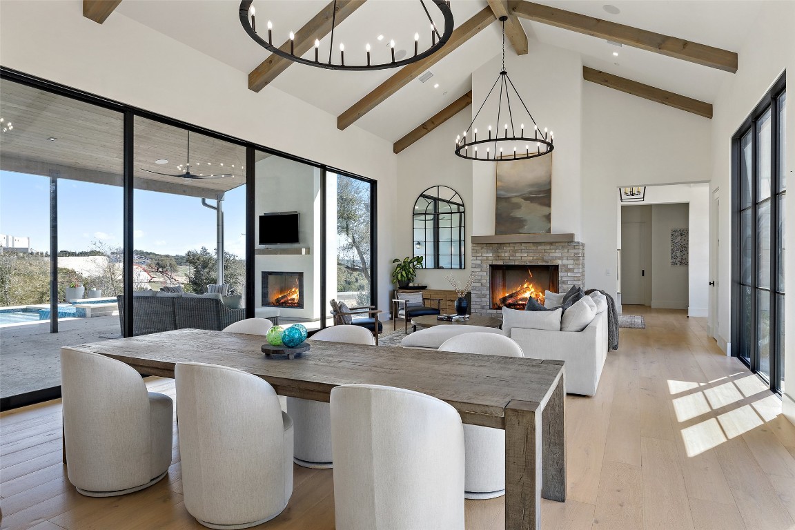 Dining room with a lit fireplace, a chandelier, beamed ceiling, high vaulted ceiling, and light wood-style flooring