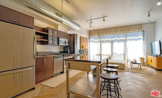 a kitchen with stainless steel appliances granite countertop a refrigerator a sink dishwasher a dining table and chairs with wooden floor