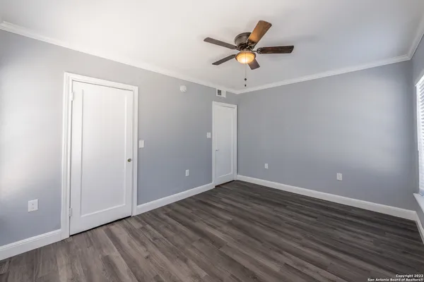a view of an empty room with wooden floor and a ceiling fan