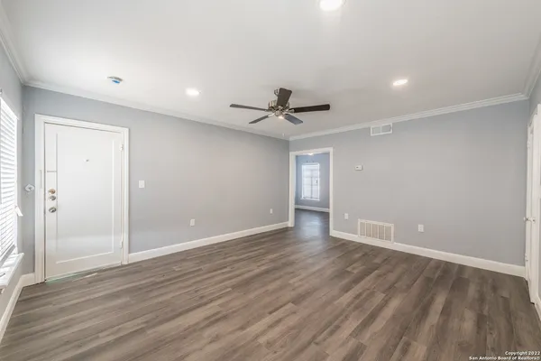 a view of an empty room with wooden floor and a ceiling fan