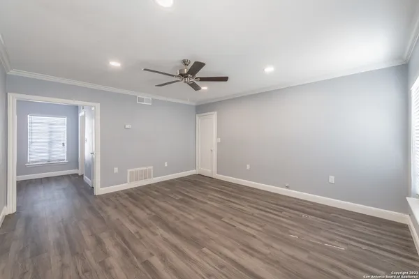 a view of an empty room with wooden floor and a ceiling fan